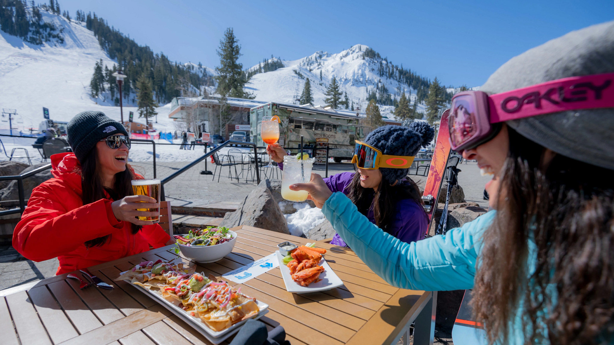 Three women sitting outdoors at Rocker on a sunny day with the slopes in the background