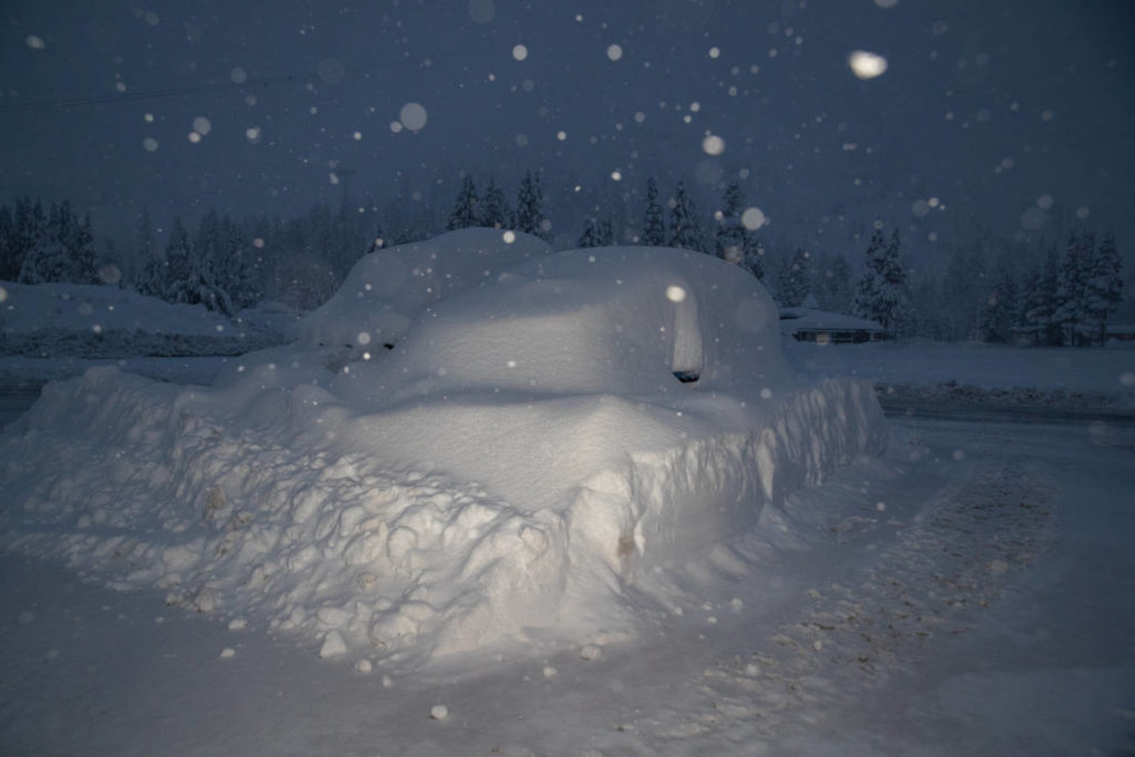 A buried car in the snowy parking lot.
