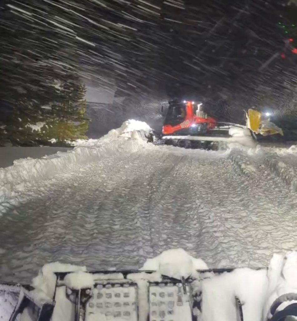 A grooming crew working in a snowstorm in the dark.