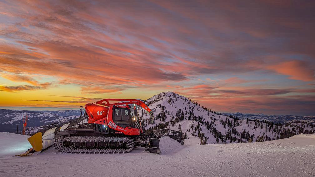 A snowcat in front of a spectacular mountain sunset.