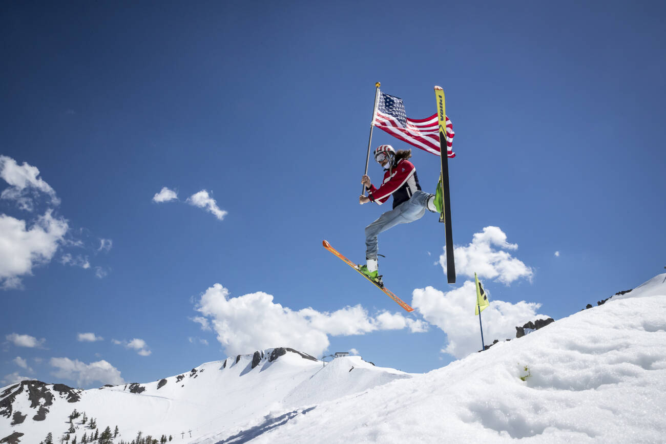A skier does a spread eagle with an American flag.