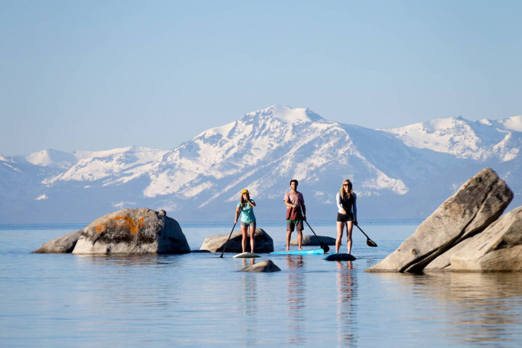 three individuals paddleboard on Lake Tahoe after a day at Palisades Tahoe. 