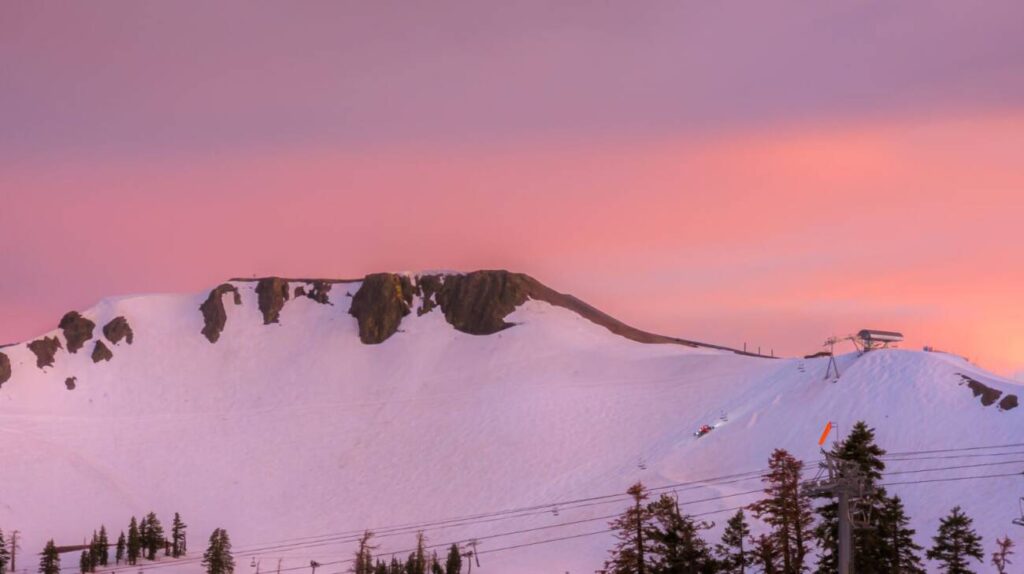 A snowcat climbing Siberia face with a view of the Palisades at sunset.