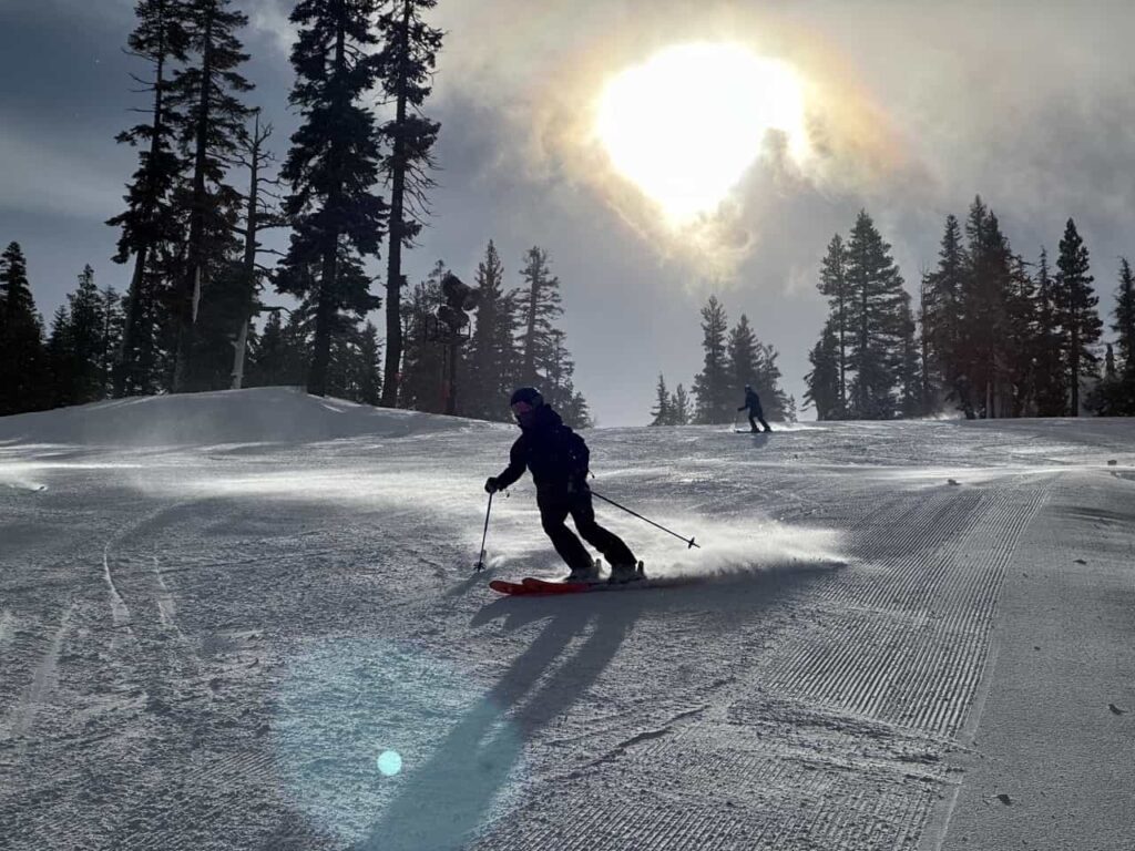 Skiing turning on groomed slope with sun behind