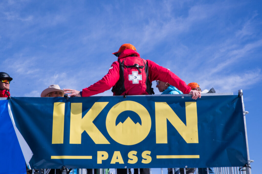 A ski patroller with an Ikon Pass banner.