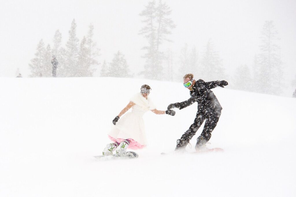 Couple in wedding dress and tuxedo snowboard down mountain in the snow at Palisades Tahoe.
