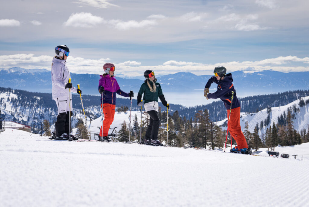 An instructor teaches three skiers with a lakeview.