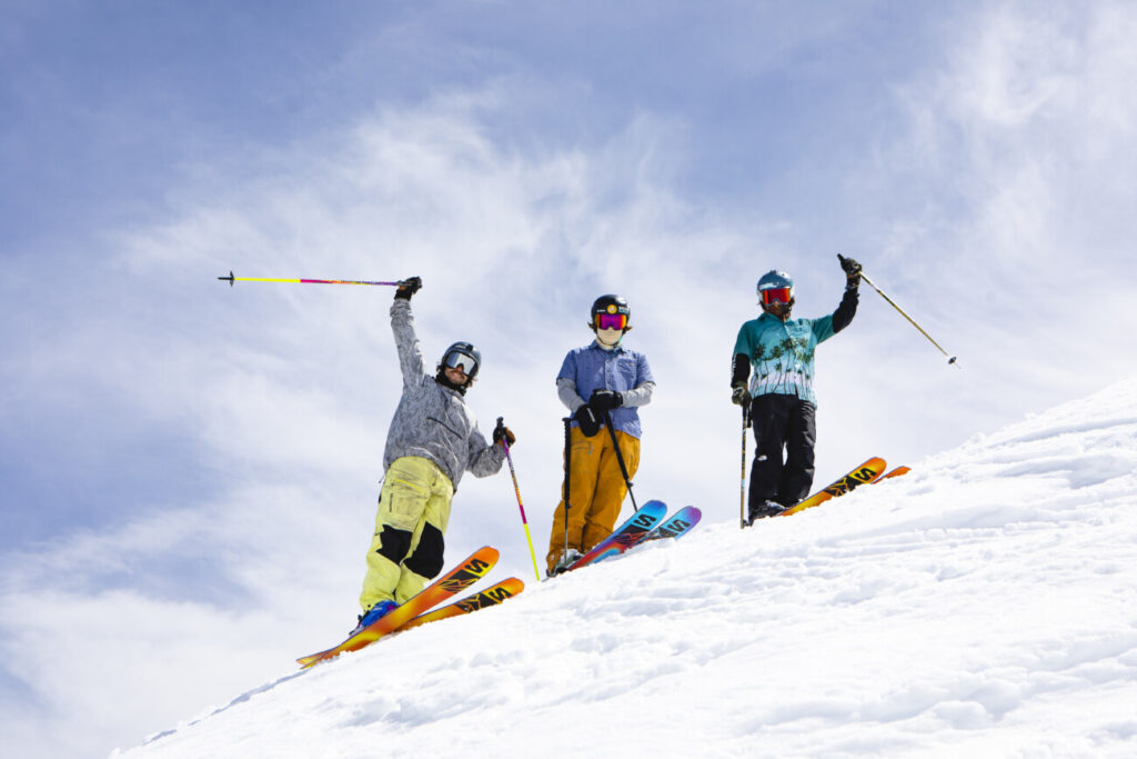 3 skiers in bright colors wave at the camera