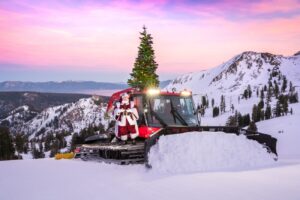 Santa standing on snow groomer with Christmas tree