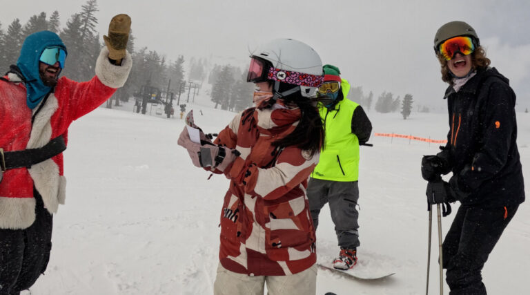 A skier wins a giveaway and celebrates with skiers in a Santa and elf costume