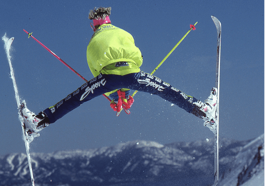 Brad Holmes in a bright green jacket with his skis at a 90 degree angle