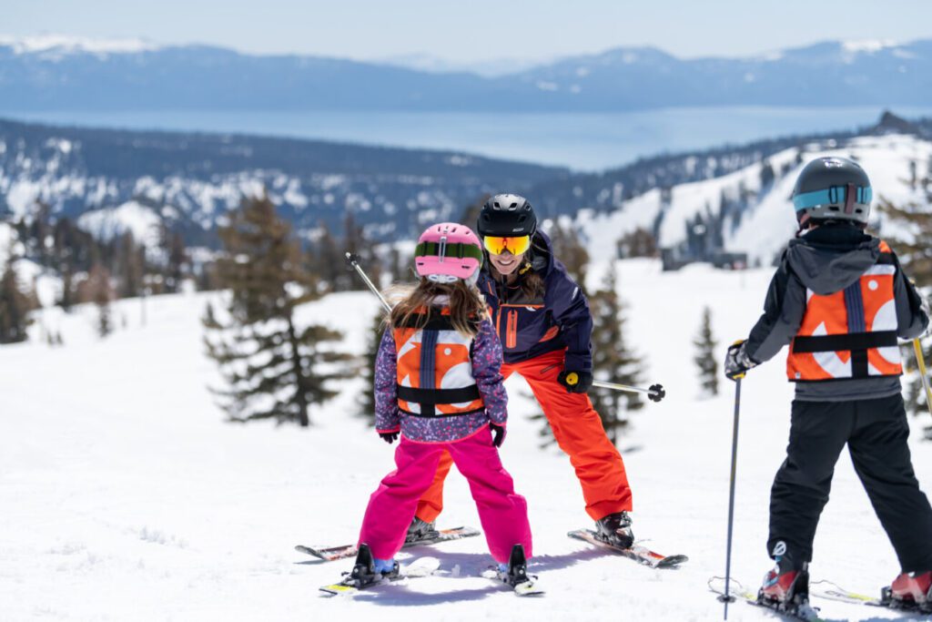 Girl and boy standing on skis with instructor with a view of Lake Tahoe