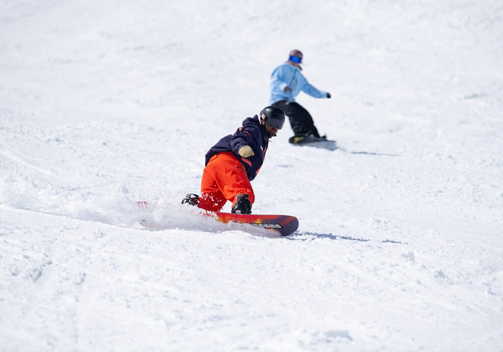 Snowboard instructor with student in blue jacket