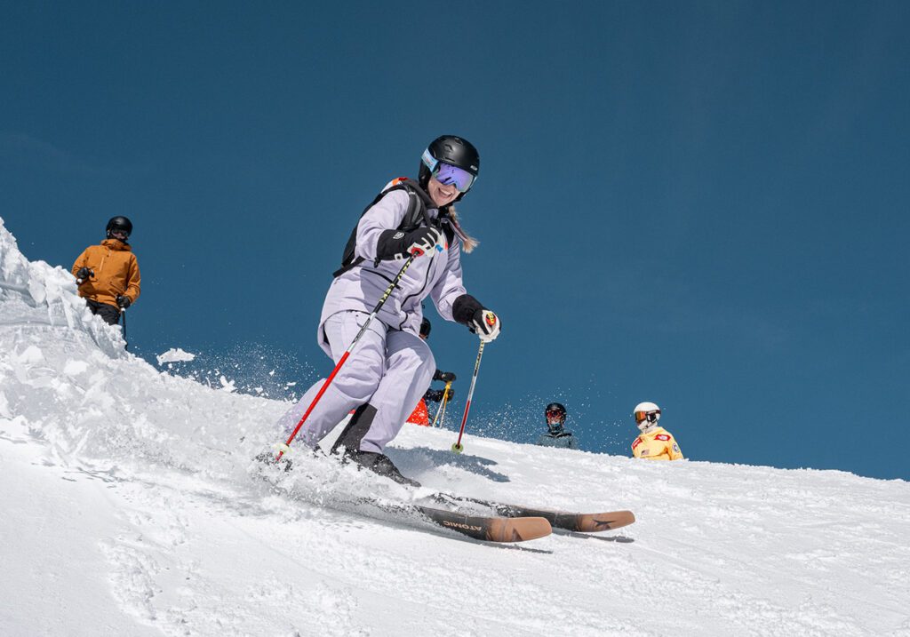 Gal in lavender ski suit smiling on her skis