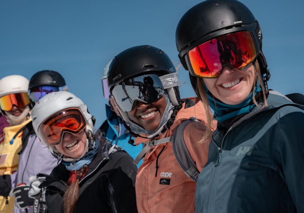 Group of gals smiling at camera in goggles and helmet